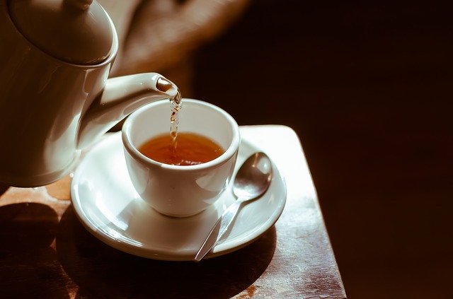 An elevated yellow tea pot pouring tea into a yellow cup/saucer on a green background