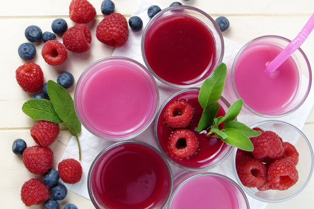 multiple clear glasses of red or rose smoothies with raspberries, blueberries and mint scattered around.